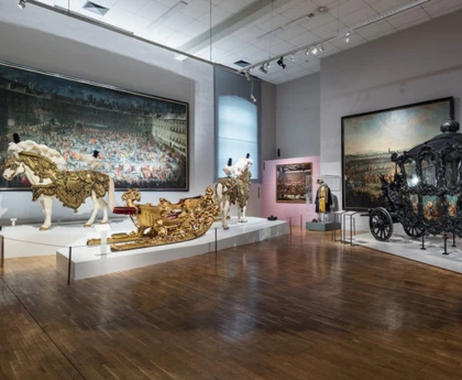Inside the Imperial Carriage Museum, showing a collection of royal carriages and intricately decorated coaches displayed in a grand, historic hall.