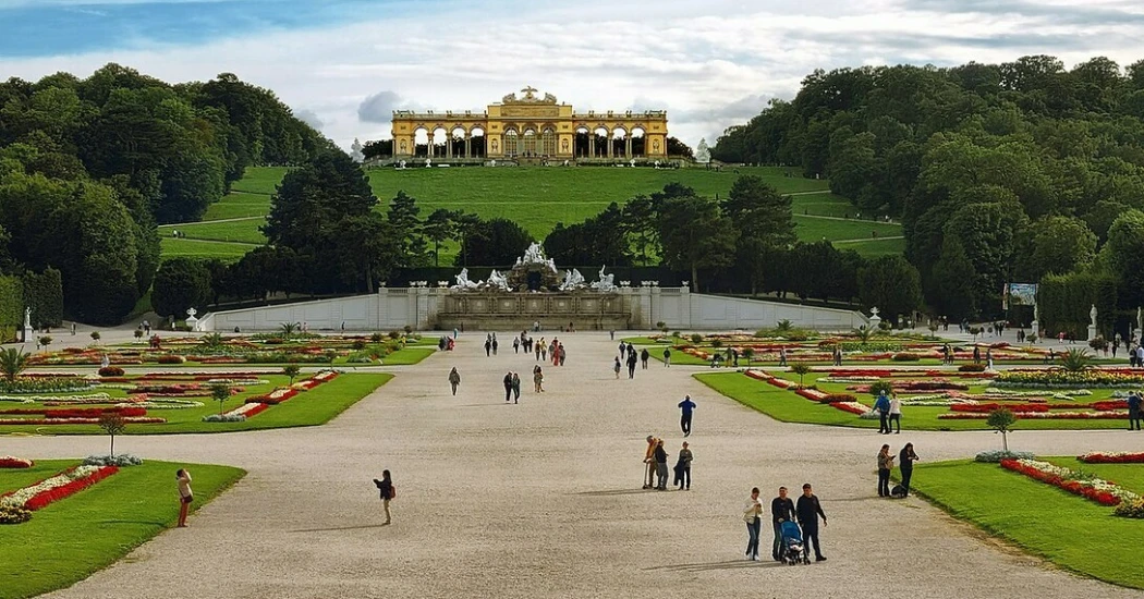 A huge courtyard with colorful gardens on the side where people are strolling and clicking pictures. 