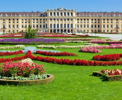 A colorful garden with multicolored flowers and green grass in front of the Schonbrunn Palace.