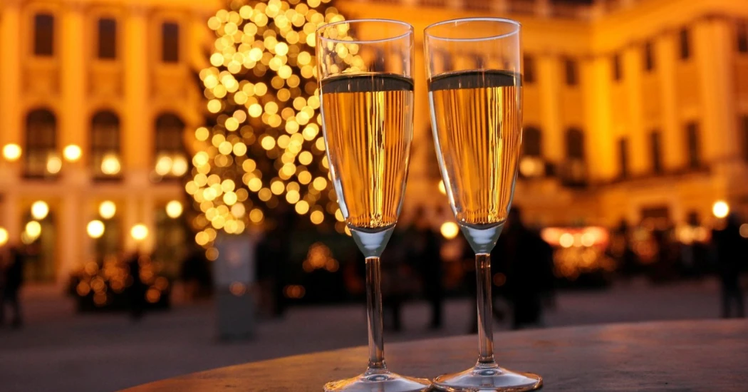 Two champagne glasses are kept on a table with a backdrop of well-lit Schonbrunn Palace.