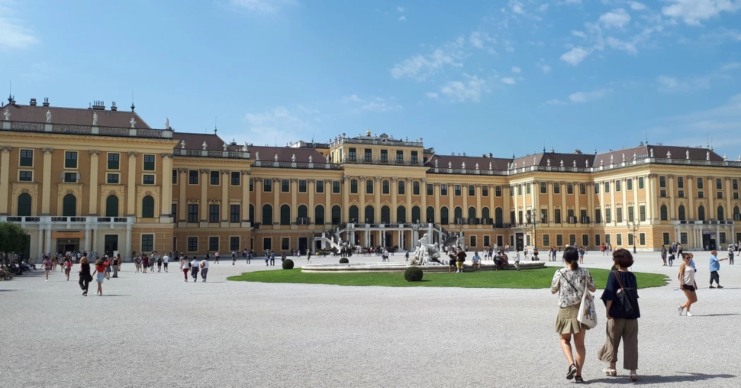 Visitors stroll through the gardens in front of the Schönbrunn Palace, showcasing its baroque architecture.
