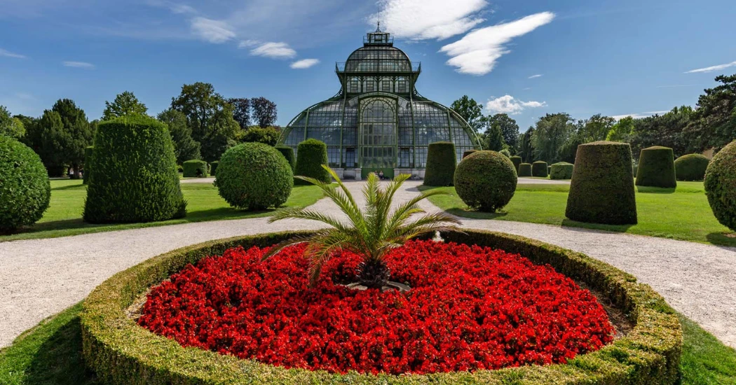 Glass Palm House in Vienna’s Schönbrunn gardens with red flowers and greenery