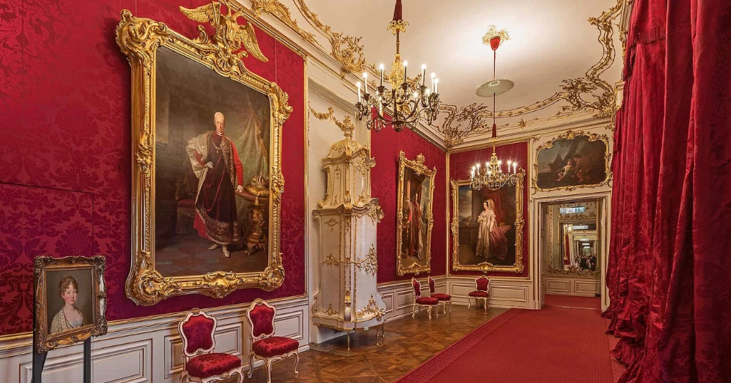 Interior of Schönbrunn Palace's royal corridor lined with Baroque paintings and velvet walls