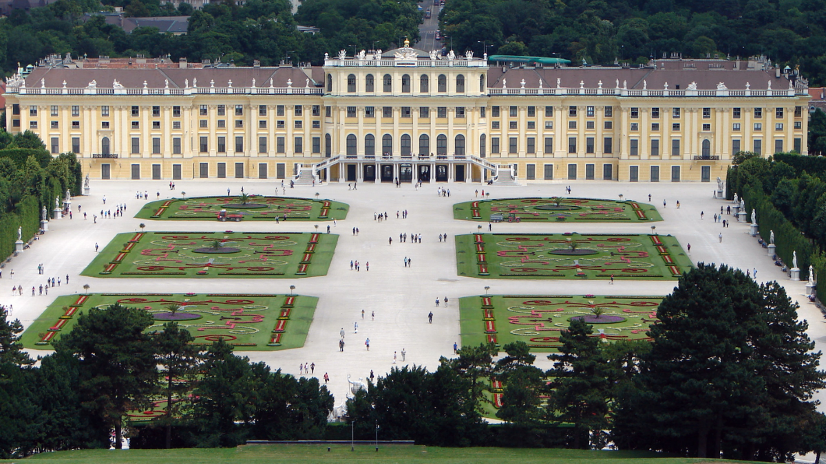 Aerial view of Schönbrunn Palace in Vienna, surrounded by symmetrical gardens and visitors exploring the grounds.
