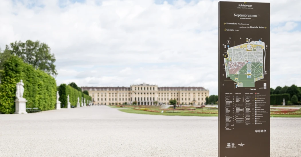 A map sign showing directions and locations inside Schönbrunn Palace gardens with the palace in the background.