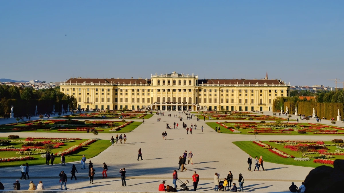 Visitors stroll through the grand courtyard of Schönbrunn Palace under a clear sky.